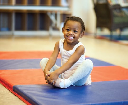 A KinderTot student sitting on a dance mat and smiling