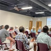 view from the back of a room where a group of senior center members are sitting in chairs listening to a presentation