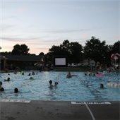 People swimming in a pool in the evening and watching a movie on a projector screen