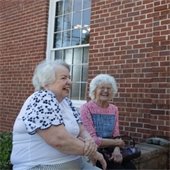 Two senior center members sitting on a brick wall laughing