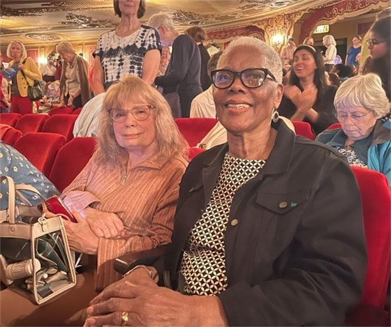 two senior center members sitting in a theater together smiling