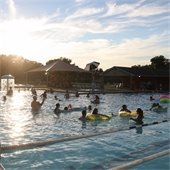A full pool at sunset with people swimming with floaties