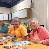 Two women smiling at a table together doing a craft