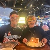 Two senior center members wearing "caketime" glasses and holding up slices of birthday cake