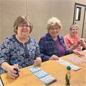 Three women sitting at a table together playing bingo and smiling