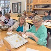 Two women baking snowball cookies together and smiling
