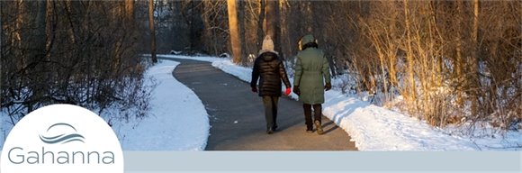 Two people bundled in winter coats walking along a cleared trail during the winter