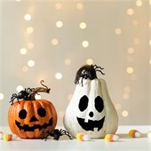 Two pumpkins with painted jack-o-lantern faces sitting on a table in front of string lights