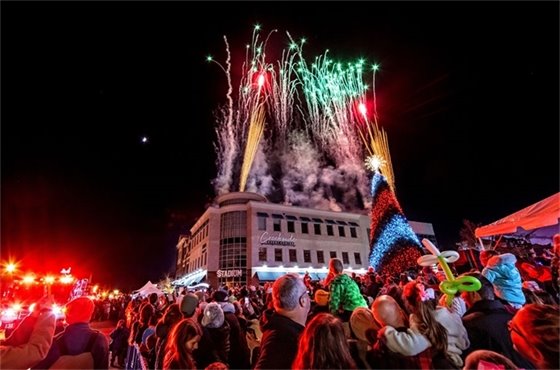 A crowd of families watching holiday fireworks go off behind a Christmas tree in Creekside