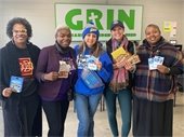 A group of five women standing in front of the GRIN (Gahanna Residents in Need) sign, smiling and holding various gift cards and donation items. 