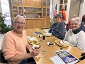 Three Gahanna Senior Center members sitting at a table, sharing a meal together and smiling.