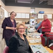 Three senior center members smiling at camera and making jewelry