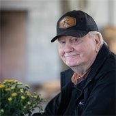 a man smiling next to a pot of mums during the fall fireside feast