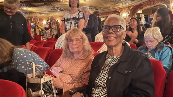 Two senior center members sitting together in a theater during a day trip