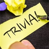 a hand holding a pen and writing the word "trivia!" on a piece of yellow paper