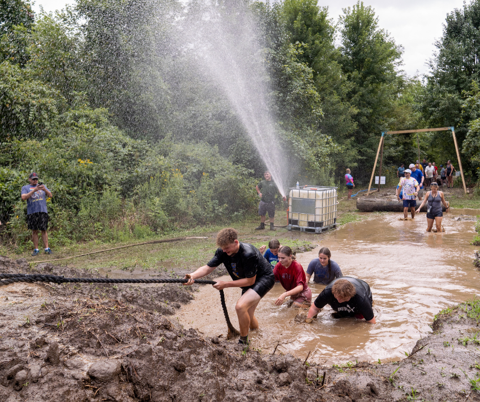 A group of people climbing out of a large muddy puddle
