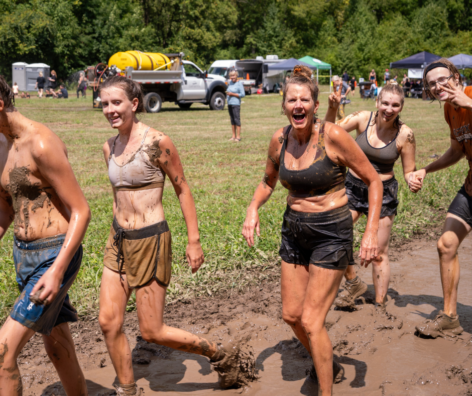A group of muddy miler participants smiling and waving as they do the obstacle course