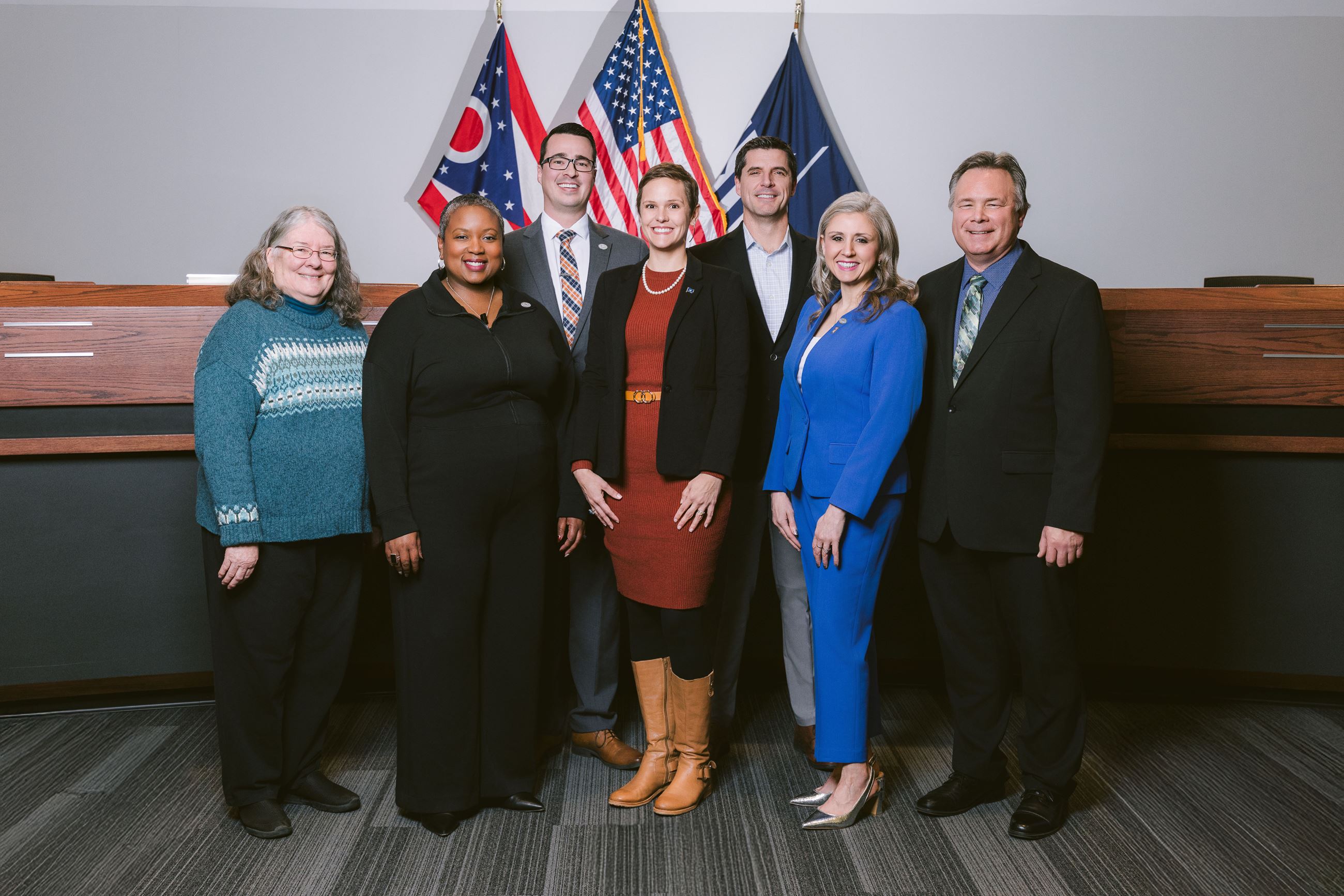 Seven members of Council stand in front of Council Chambers dais, smiling at the viewer.